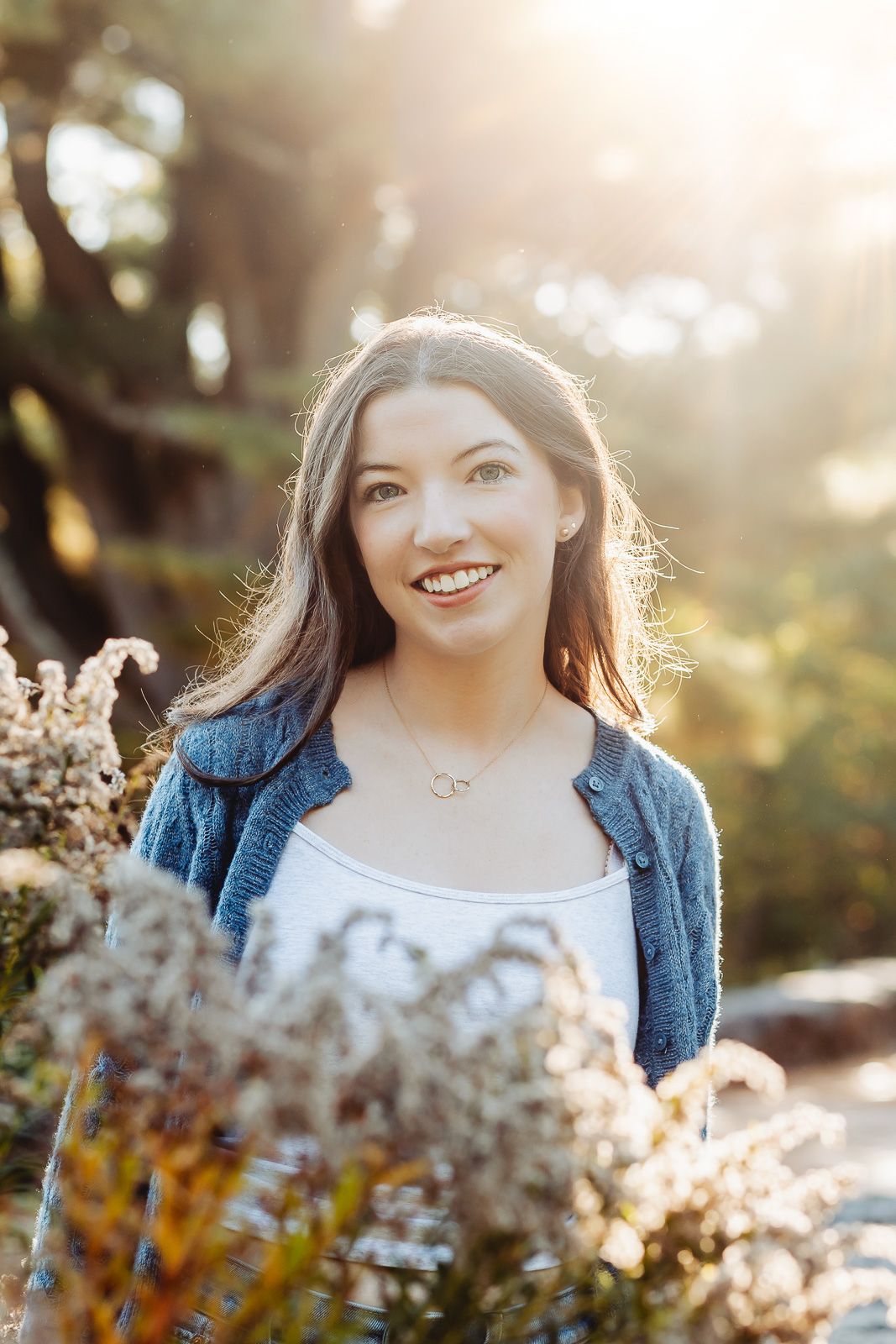Sunlit outdoor portrait with soft bokeh effect and dried flowers in the foreground creating a dreamy atmosphere.