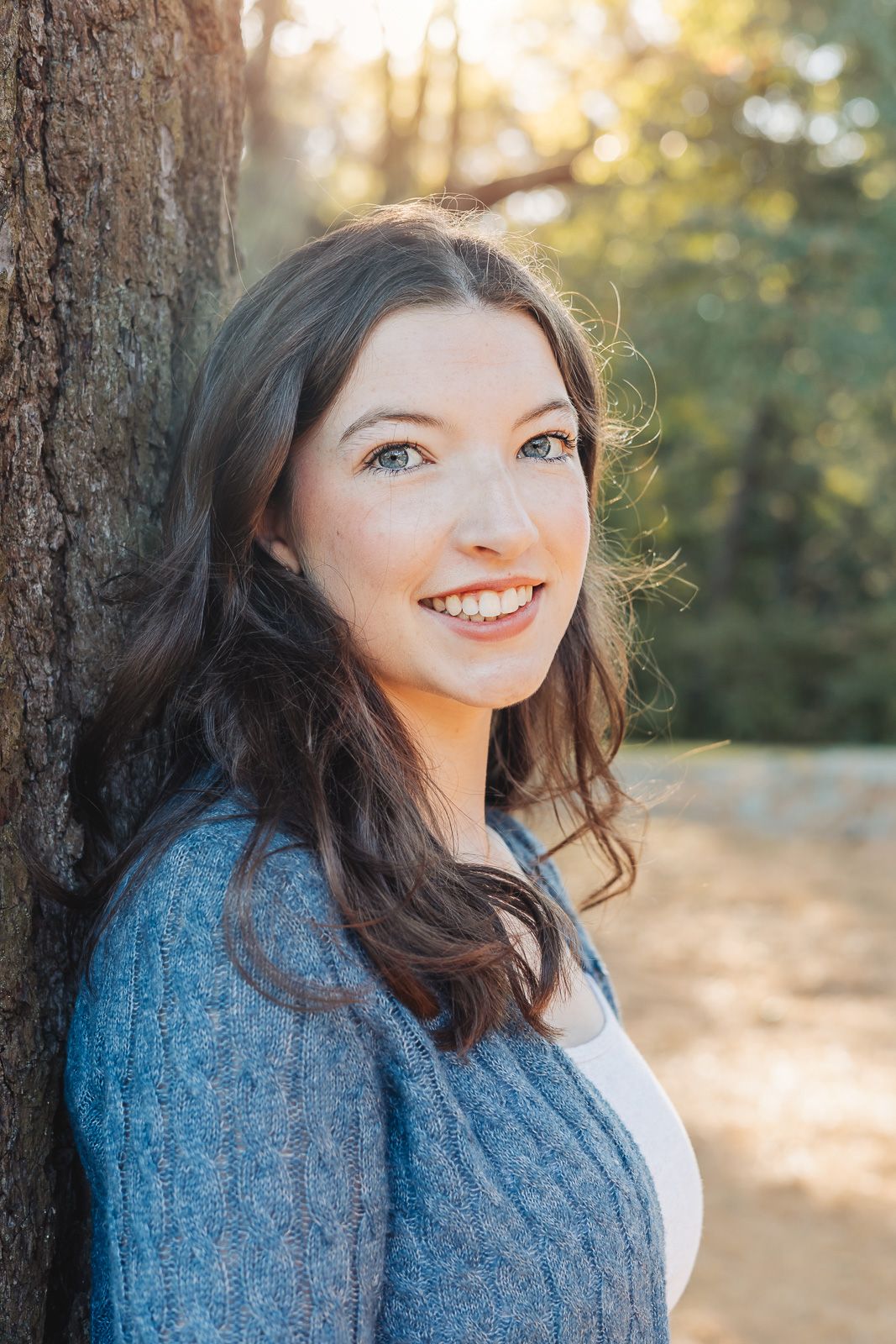 Portrait series showing a person in a blue sweater against a tree trunk with natural sunlit background.