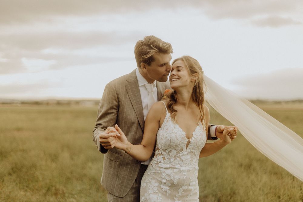 A couple shares an intimate moment in a golden field at sunset while the bride's veil flows in the wind.