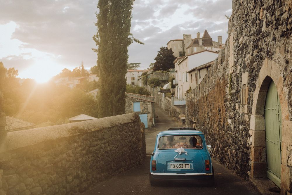 Vintage blue Fiat 500 parked on a charming cobblestone street in Italy at sunset with stone walls and cypress trees.