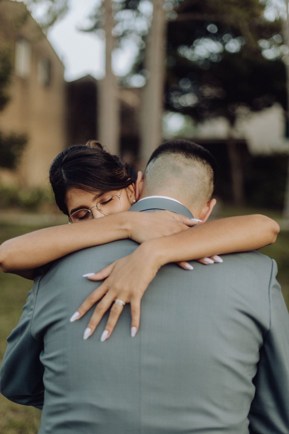 A couple embraces in a tender moment outdoors, with one person wearing a sage green outfit and the other resting their head.