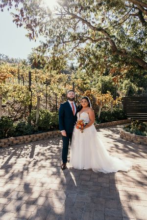 A couple poses for wedding photos on a stone patio with sunlit trees creating a beautiful autumn backdrop.