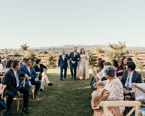 Wedding guests gather on a grassy hilltop overlooking a scenic desert landscape during an outdoor celebration.