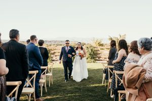 Panoramic view of an outdoor wedding ceremony with guests seated on wooden chairs during golden hour.