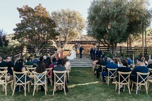 Rows of cross-back wooden chairs set up for an outdoor wedding ceremony with natural landscaping.
