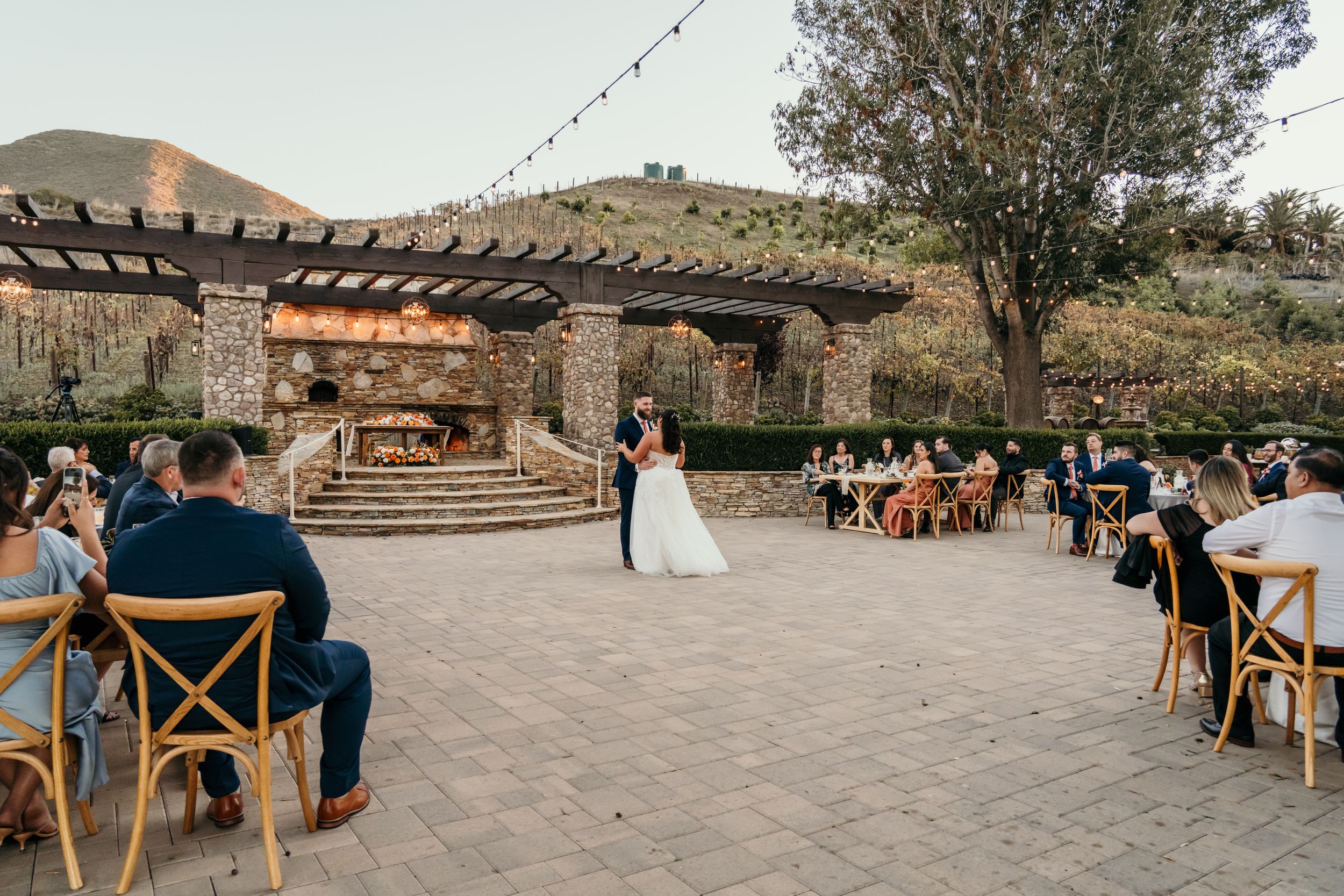 Outdoor wedding ceremony at a rustic venue with string lights and mountain views in the background.