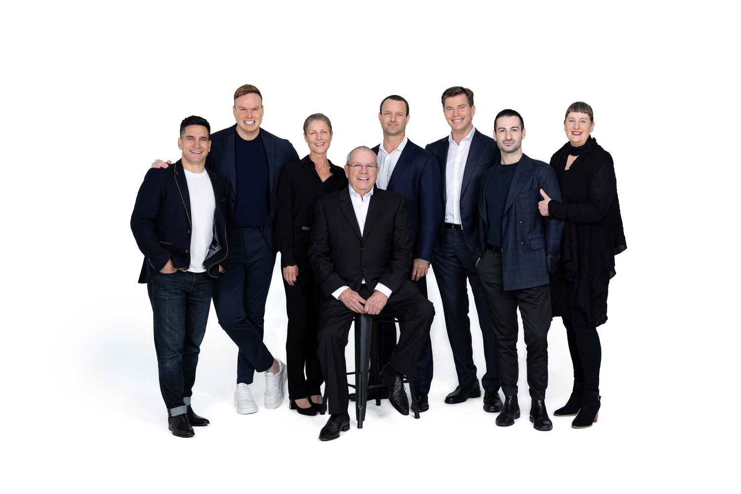 A group of business professionals in dark suits and formal attire arranged in a line against a white background.