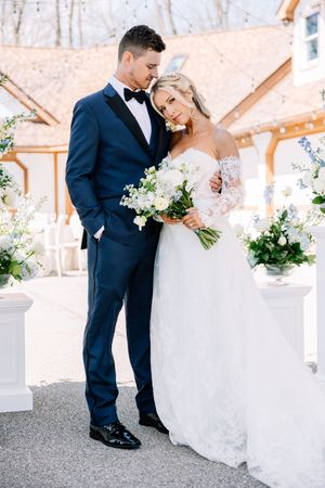 Wedding couple sharing an intimate moment near white floral arrangements at an outdoor venue.