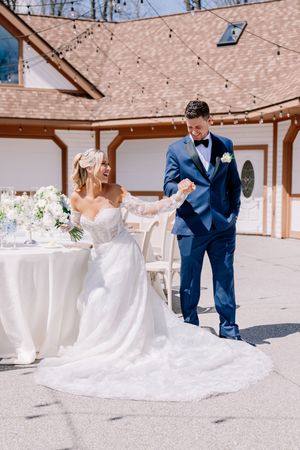 A bride in a lace gown dances with her groom on an outdoor patio.