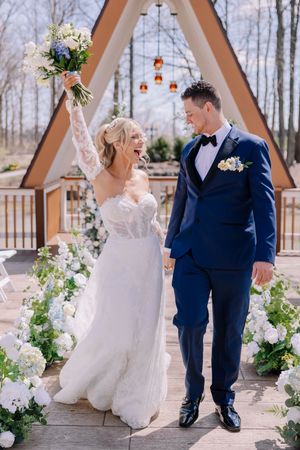 Newlyweds sharing joyful moment in front of A-frame chapel with floral arrangements.