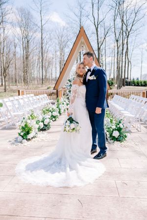 An elegant outdoor wedding ceremony setup with white chairs and floral arrangements at a rustic A-frame venue.