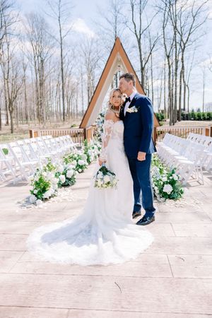 Wedding couple posing in front of A-frame chapel with white floral decorations.