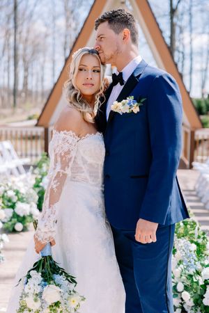 A wedding couple poses in front of a triangular chapel with floral decorations.