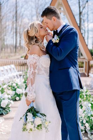 A romantic wedding moment captured at an outdoor A-frame chapel decorated with white and green floral arrangements.