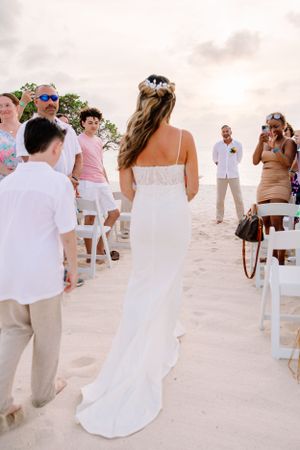 Beach wedding ceremony setup with guests seated on white chairs in the sand.