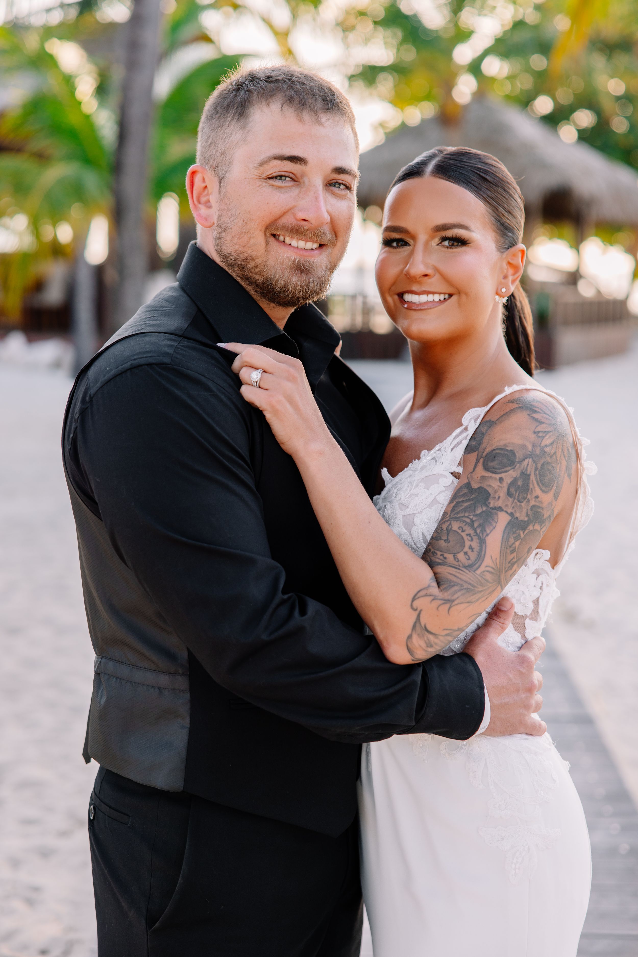 Couple in formal wedding attire embracing outdoors with visible tattoo artwork.