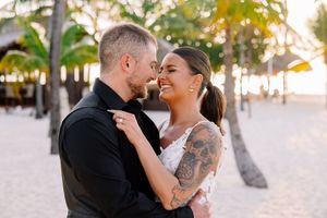 A couple embraces on a tropical beach with palm trees at sunset.