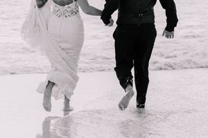 A black and white photo of a couple running barefoot on a beach.