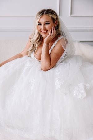 Bride in white wedding gown sitting and smiling with flowing veil.