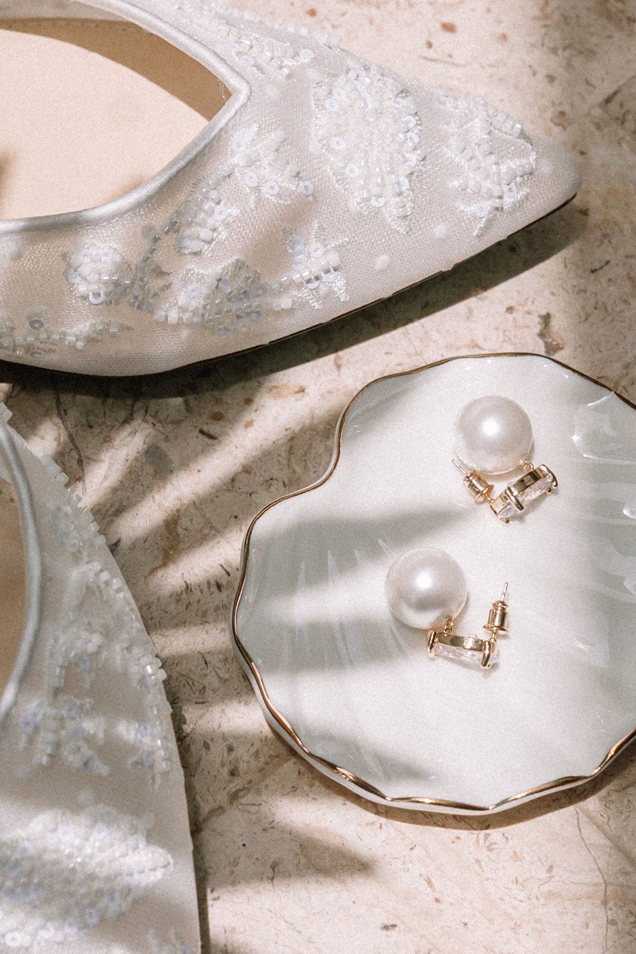 Wedding accessories including pearl earrings and rings arranged on white lace fabric.
