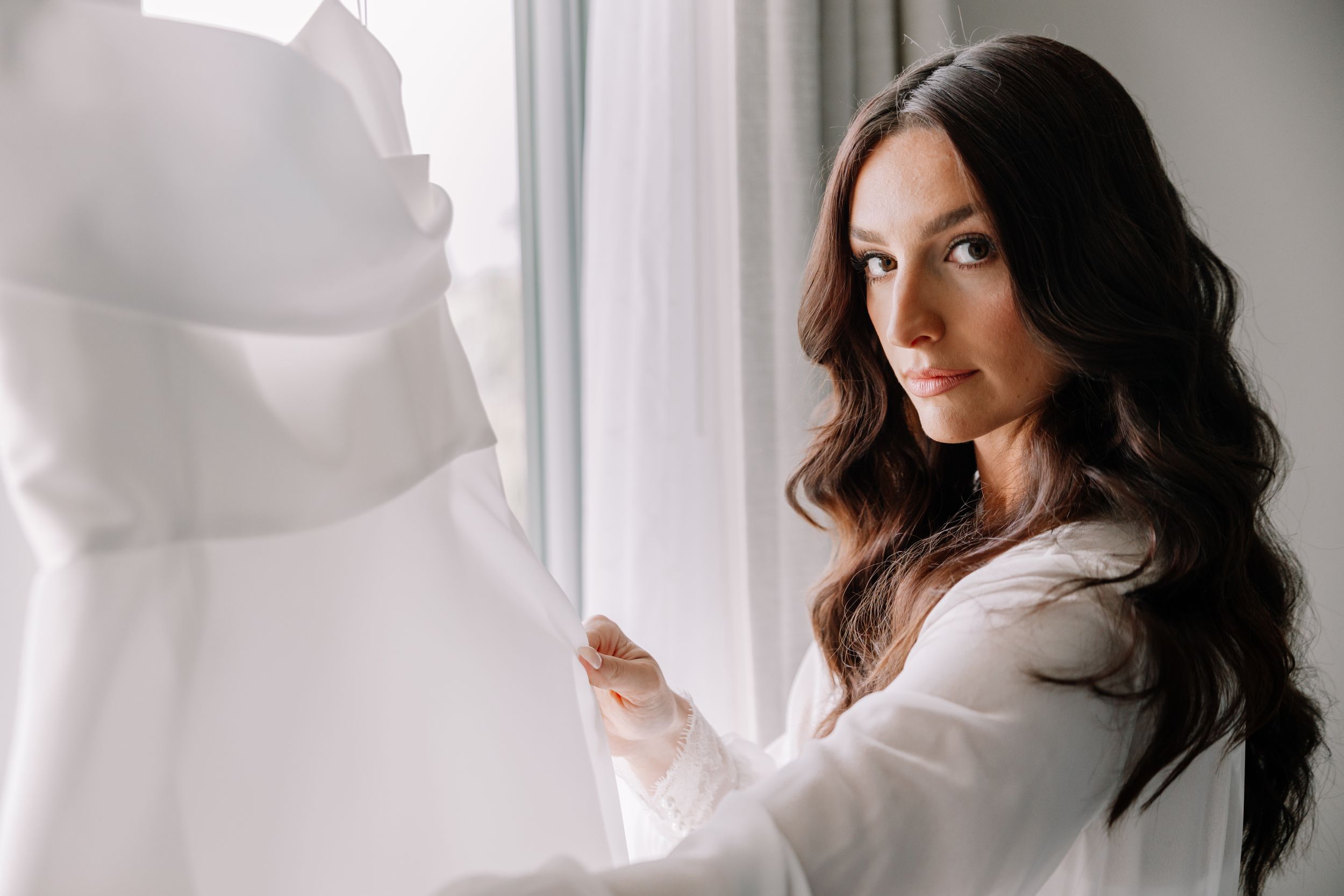 Ethereal bridal portraits near a bright window with flowing white fabric.