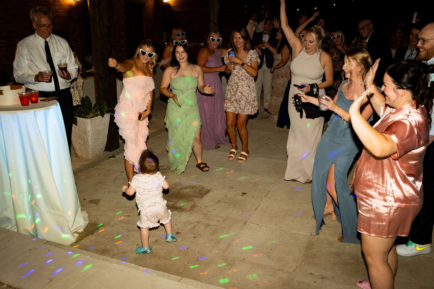 Party guests dancing on a tiled floor with colorful disco lights at an evening celebration event.