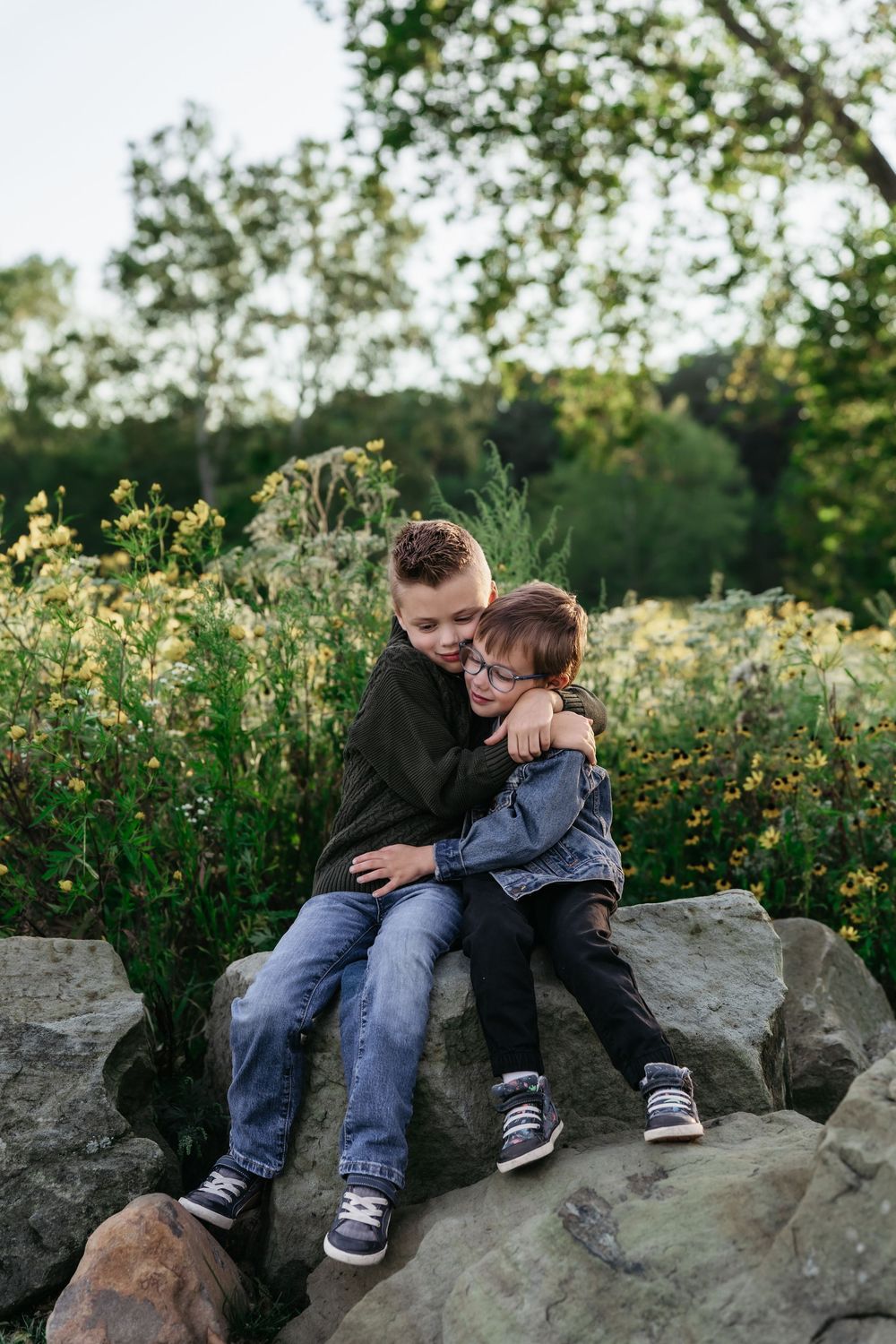 Two people share a tender moment while sitting on large rocks surrounded by wildflowers at Akron, Ohio Cascade Valley Metro Park Family Pics