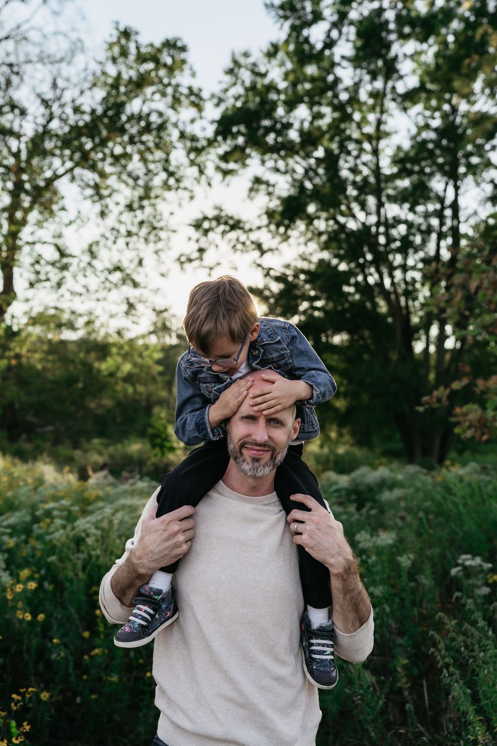 A parent in a white sweater playfully carries a child on their shoulders in an outdoor natural setting in Akron, Ohio Family Photo Session