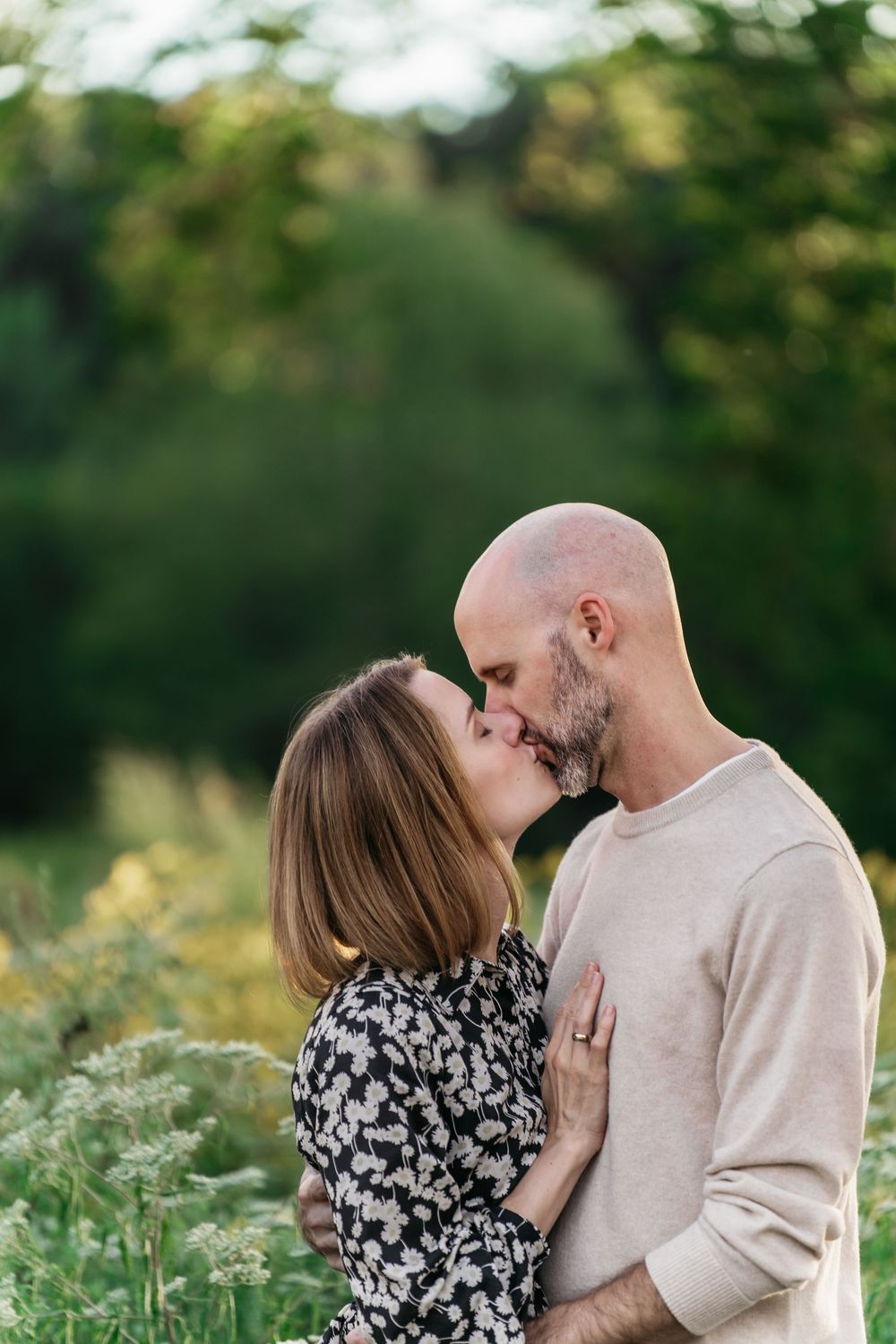 A romantic couple embraces in a sunlit meadow wearing casual attire during a tender outdoor family photoshoot in Akron, Ohio Metro Park
