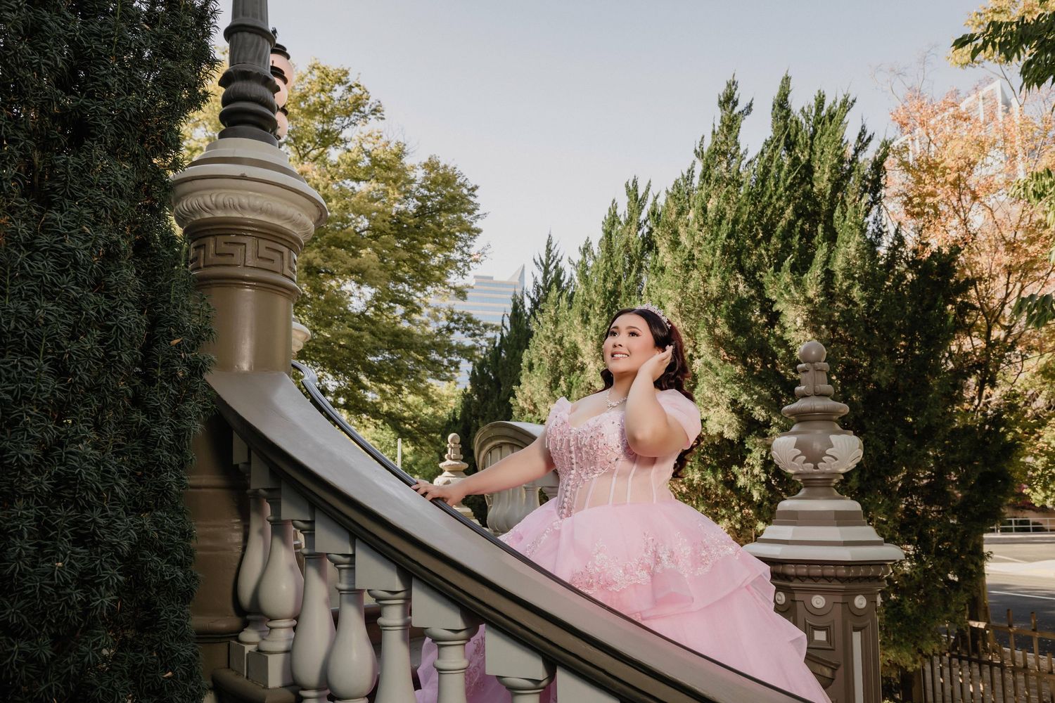 Elegant pink quinceañera gown with lace details photographed in front of a grand historic building exterior.