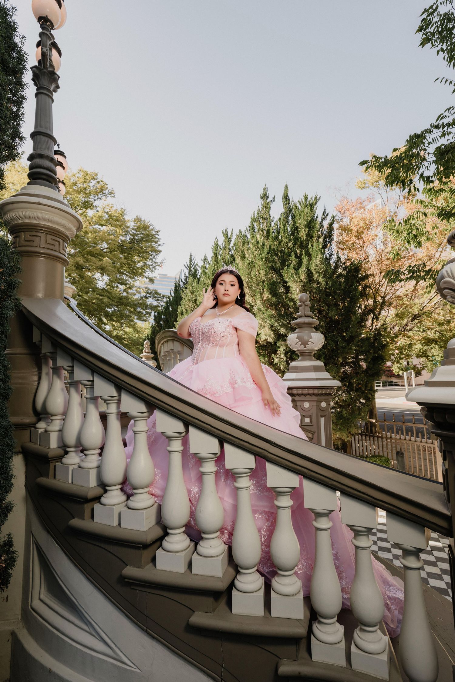 A flowing pink quinceañera dress cascades down white stone balustrades in an outdoor setting.