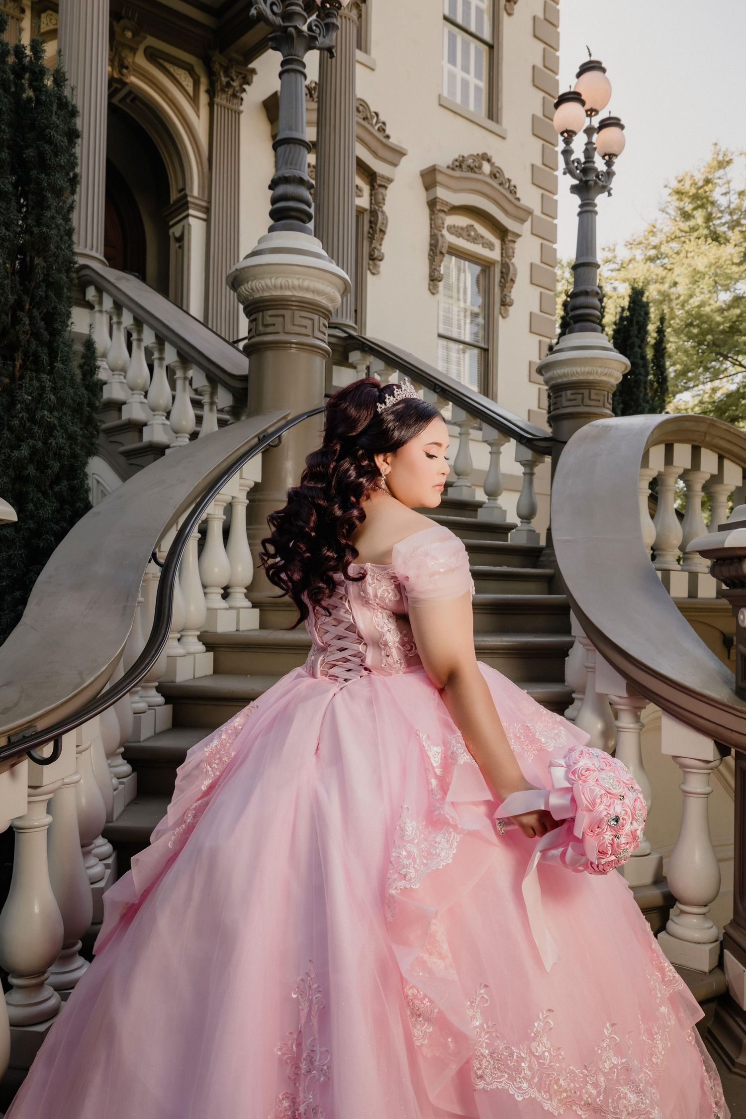 Ornate pink quinceañera dress with delicate lace details displayed on classic architectural staircase.