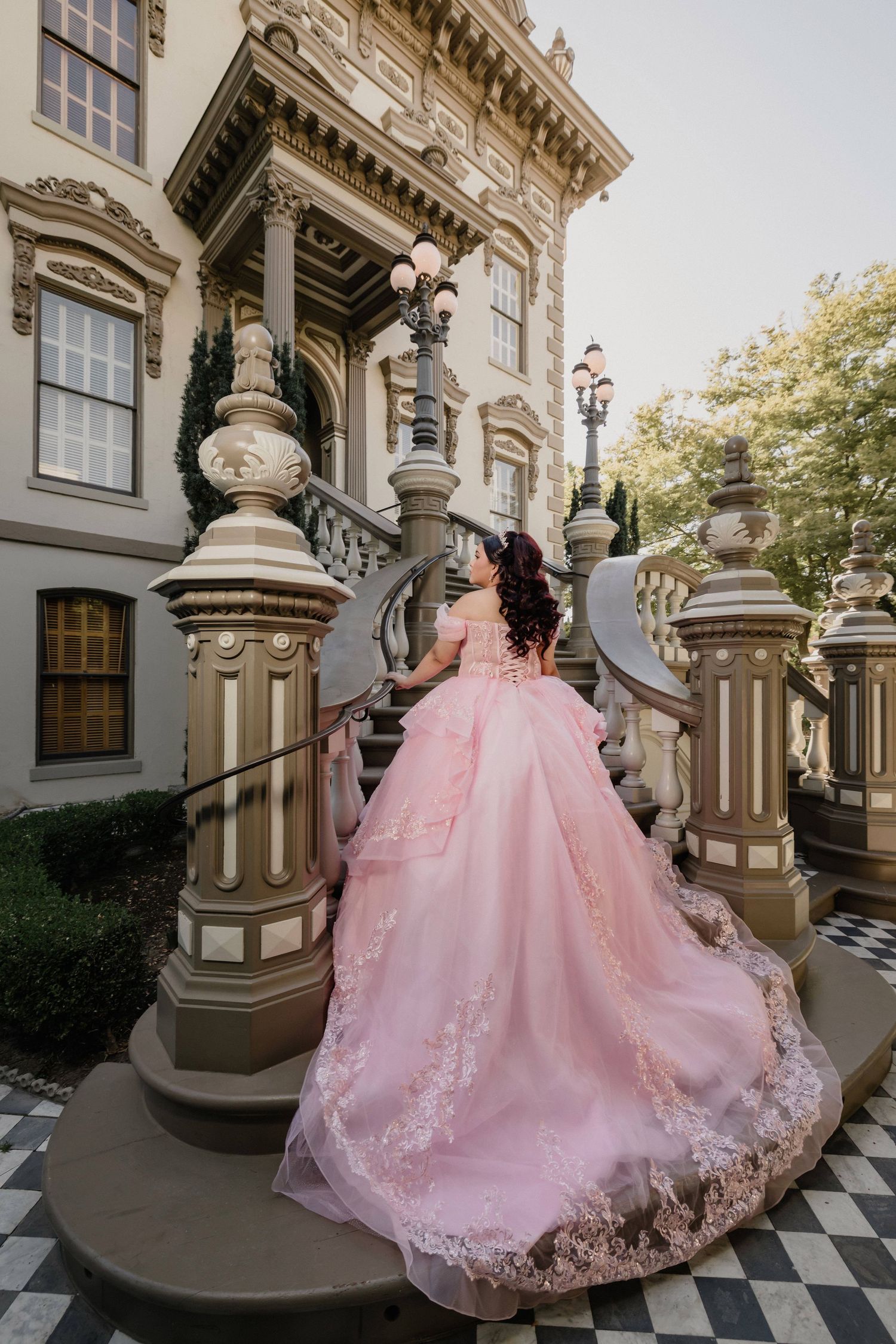 A pink ballgown dress photographed on a grand staircase with checkered floors and ornate architecture.