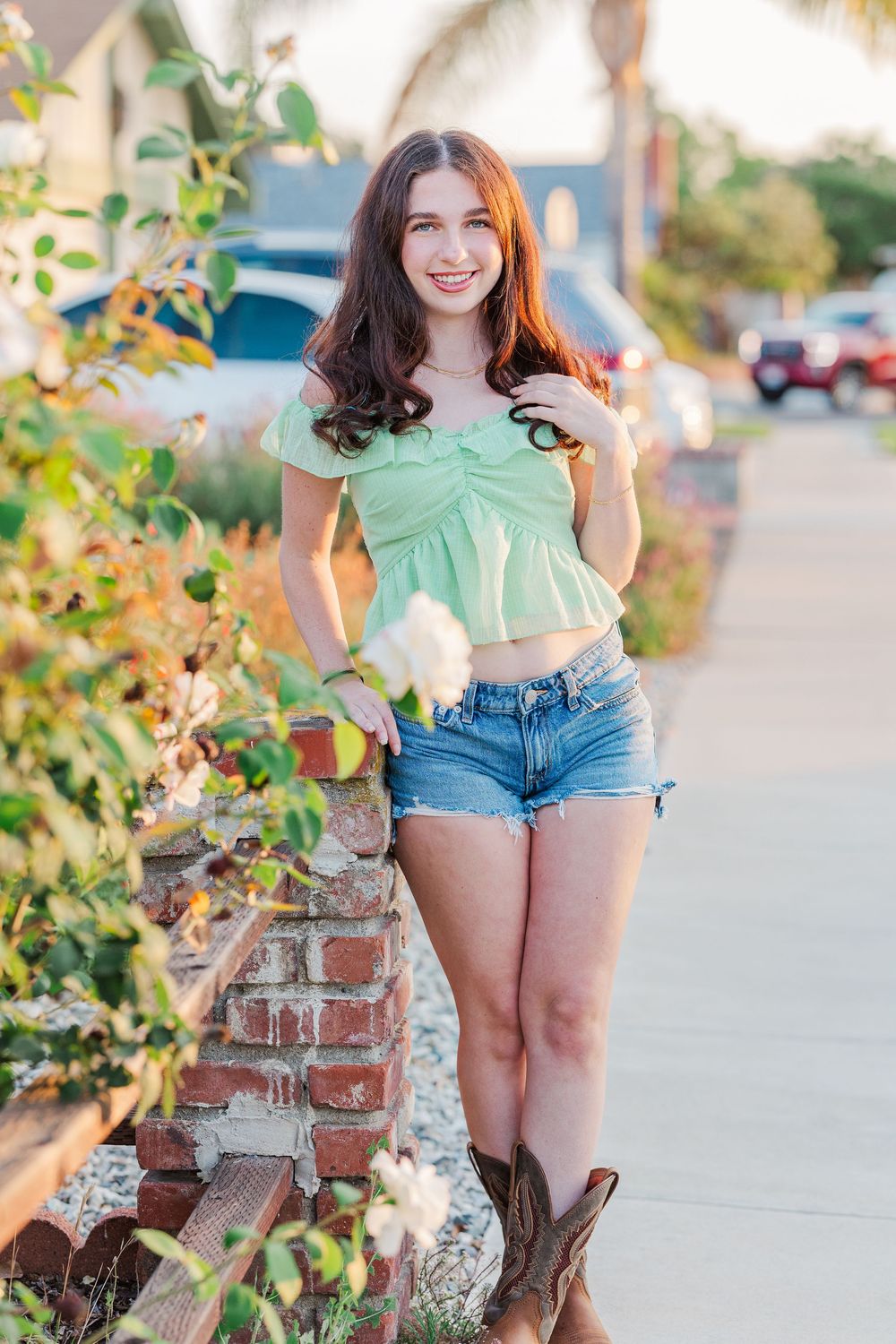 A summer portrait by a brick wall with greenery wearing a mint top and denim shorts.