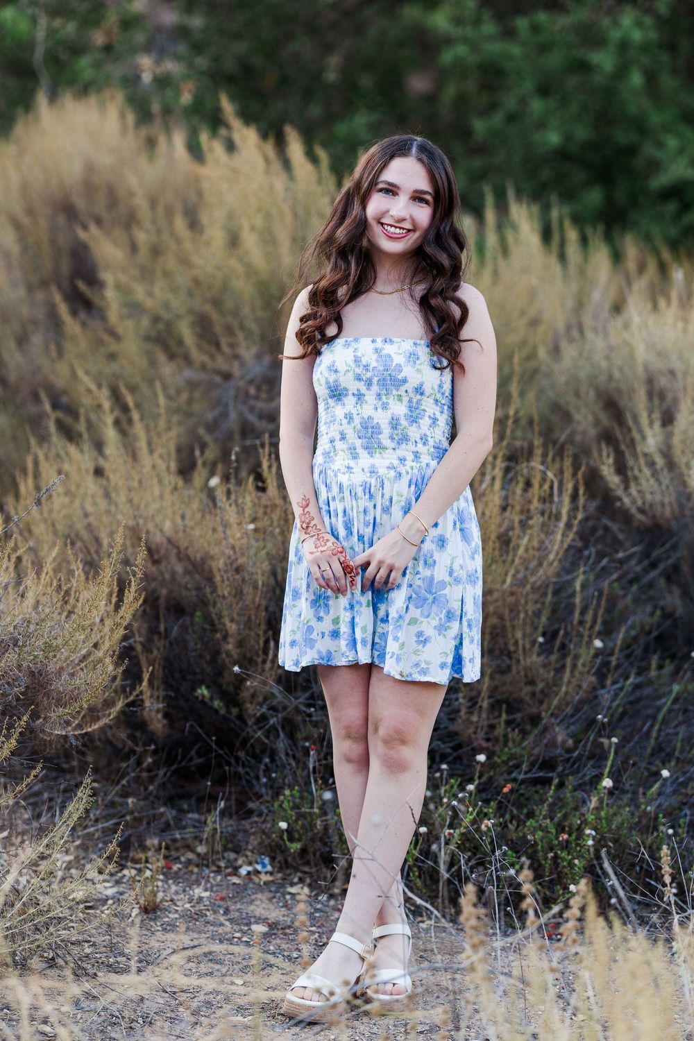 A blue floral summer dress is showcased against a backdrop of tall dry grass in a natural outdoor setting.