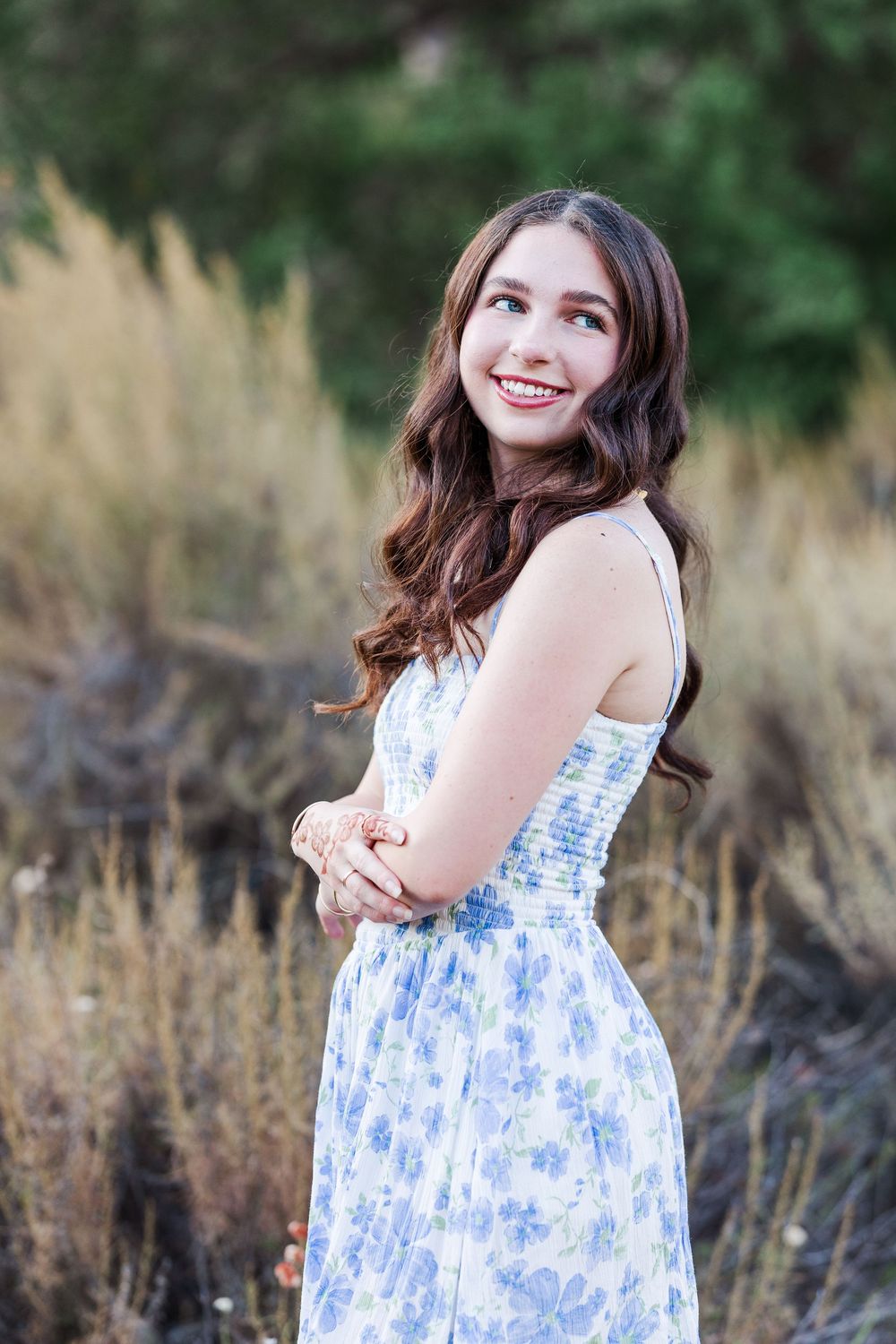 A person in a blue and white floral dress poses outdoors in a field during golden hour.
