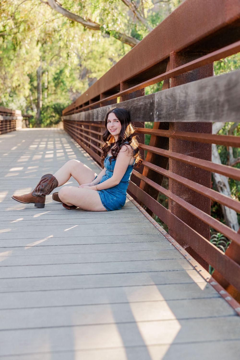 A relaxed portrait on a wooden bridge wearing denim and boots in natural lighting.