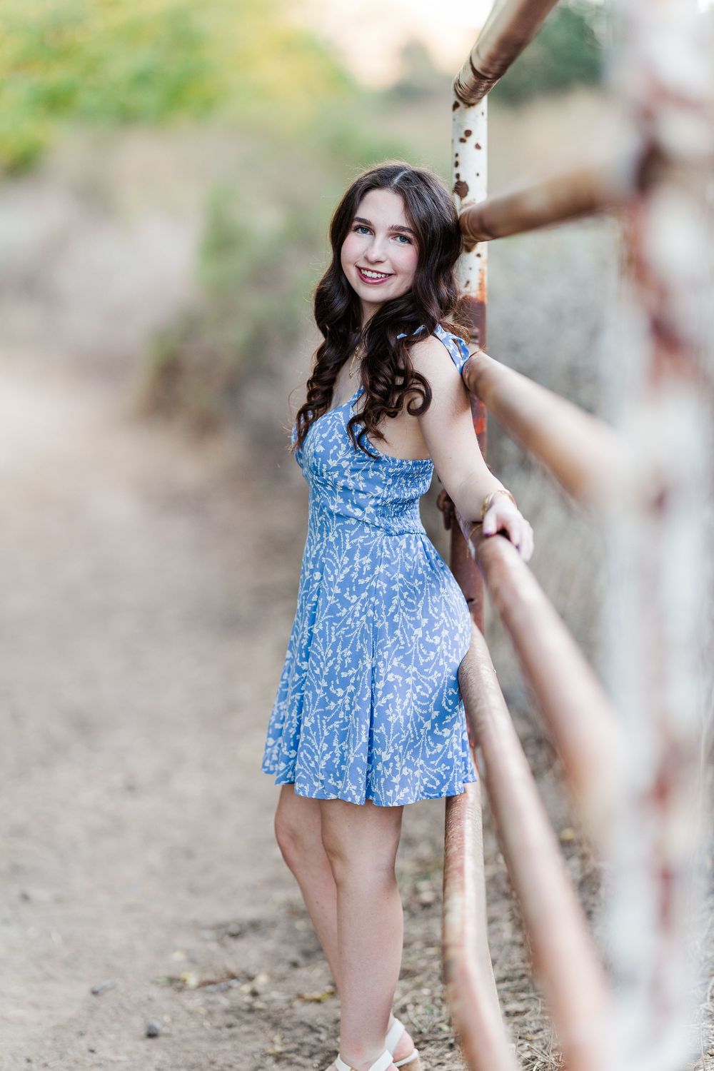 Person in a blue floral dress poses outdoors against a blurred natural background.