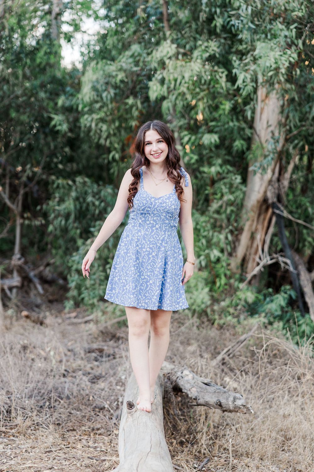 Person wearing a blue floral sundress stands in front of eucalyptus trees on a sunny day.
