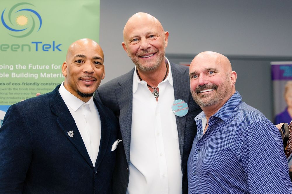 A group of business professionals posing together at a corporate event with a green and blue logo visible in background.