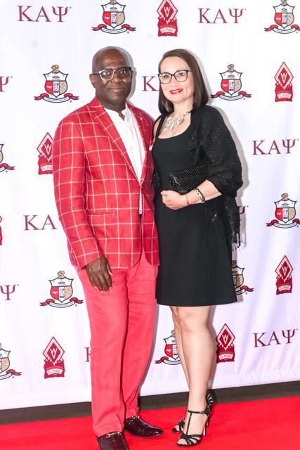 Attendees in red and black formal wear stand on a red carpet with Kappa Alpha Psi branding.