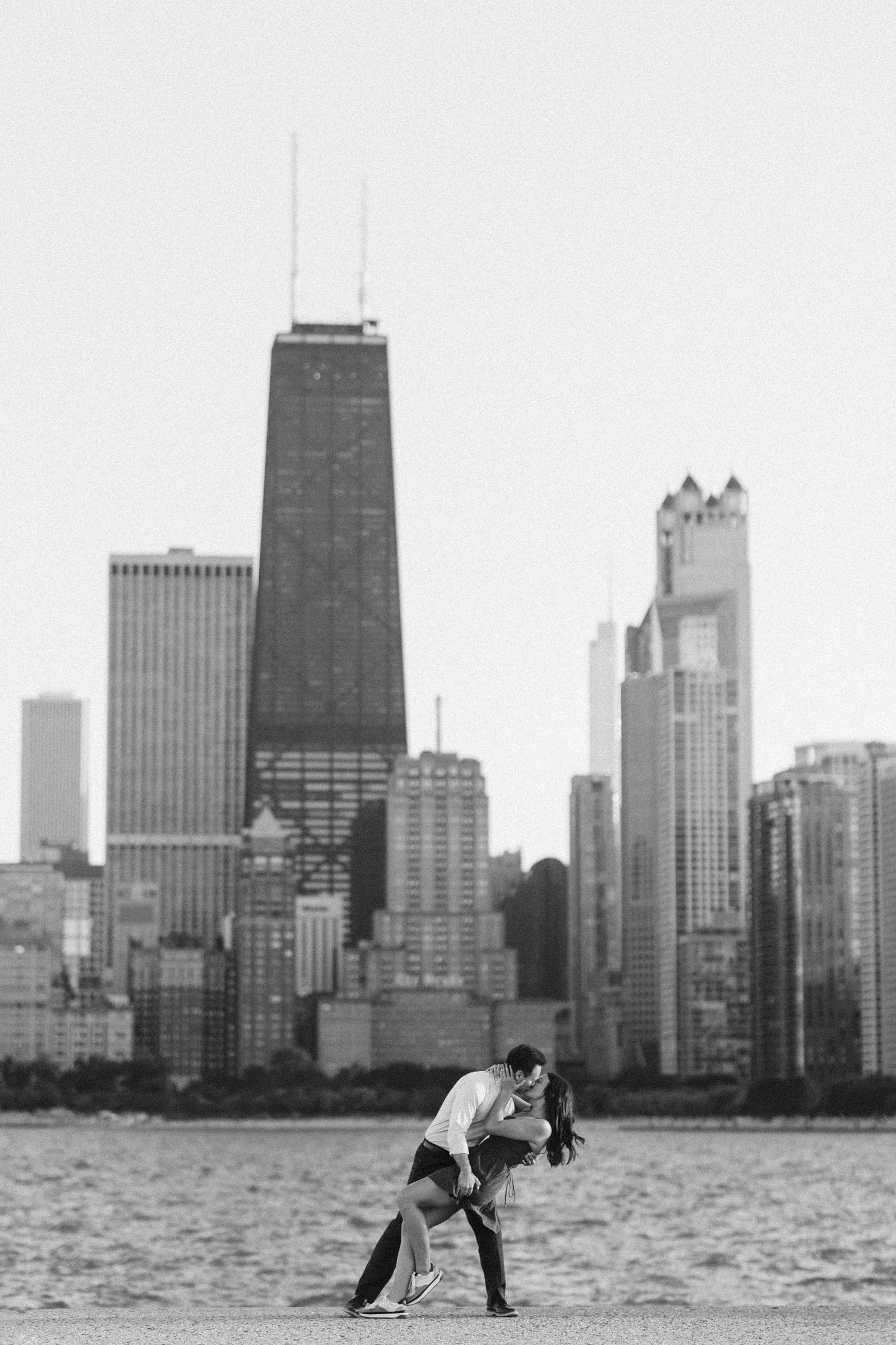Black and white photo of couple in romantic pose with Chicago skyline across the water.