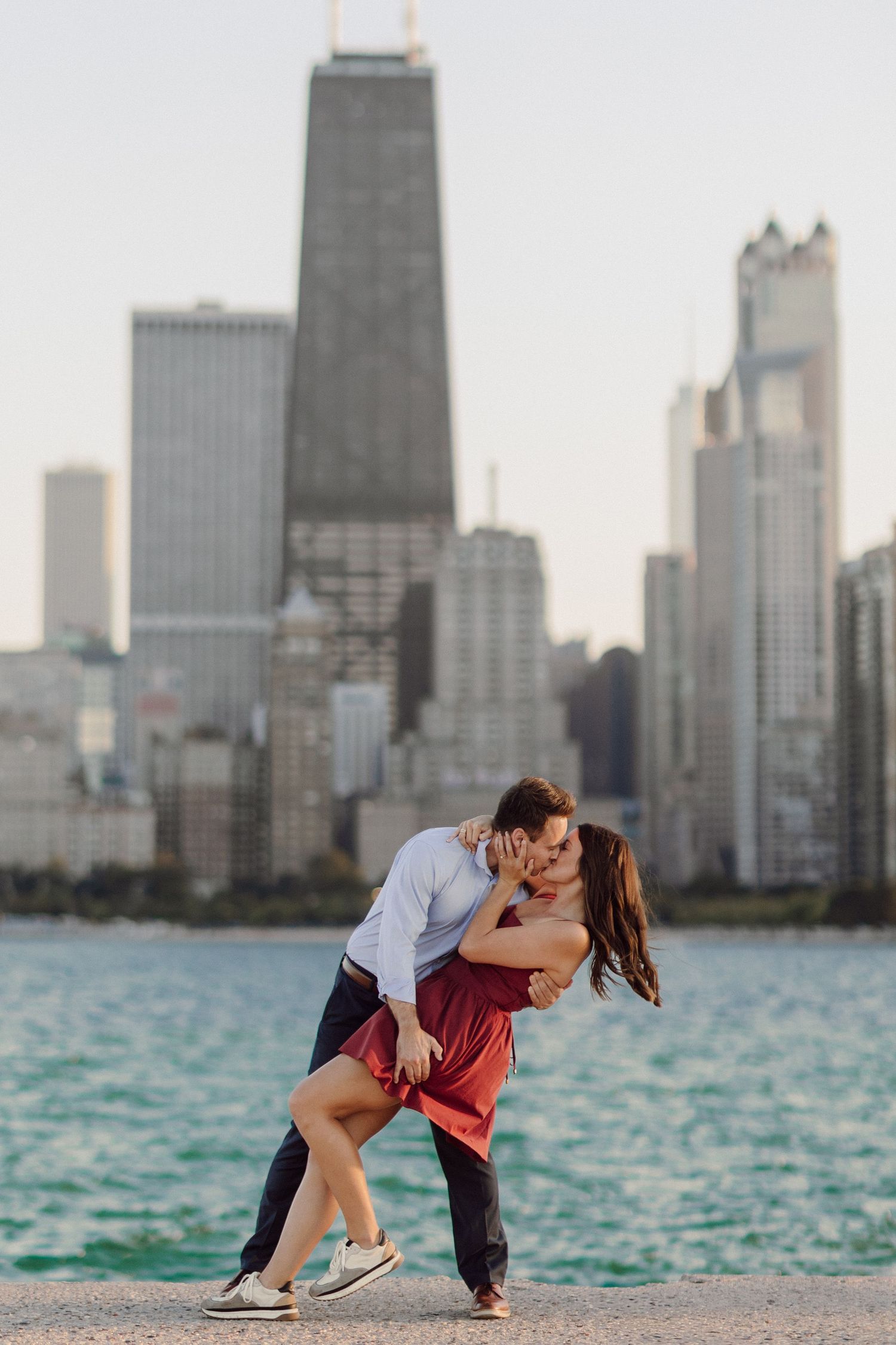 Romantic couple poses against Chicago skyline backdrop during sunset over Lake Michigan.