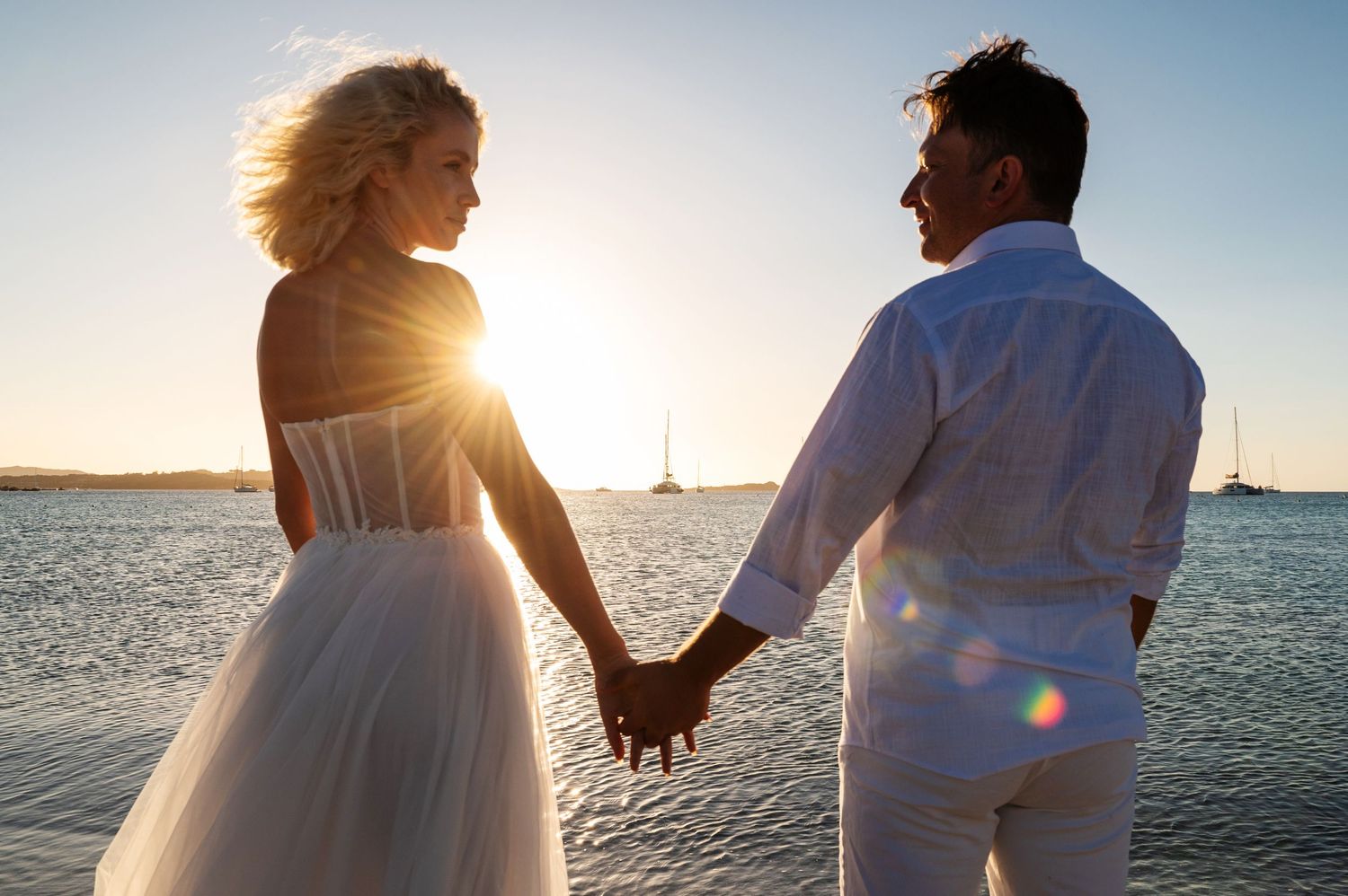 Couple walking along beach shoreline during golden hour sunset.