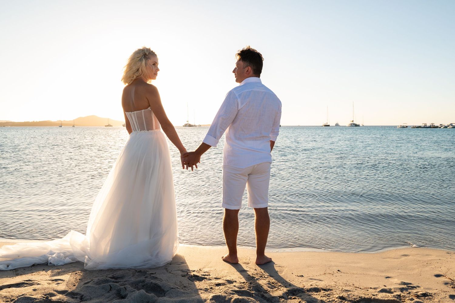 Romantic beach photoshoot with couple holding hands at sunset by the ocean.