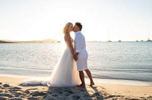 Couple shares intimate moment on sandy beach with ocean waves in background.