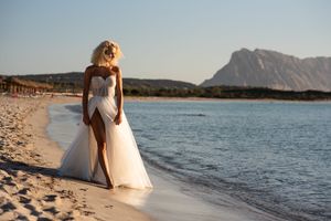 A white wedding dress flows in the ocean breeze as waves lap at the sandy beach shore.