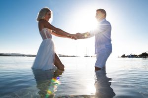Silhouettes of a couple standing in shallow water during golden hour at the beach.