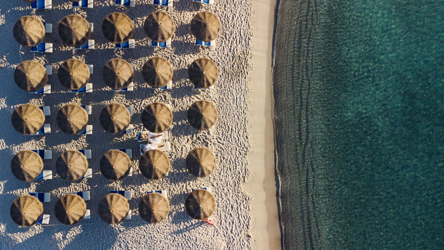 Aerial view of beach umbrellas and loungers arranged in rows along turquoise waters.
