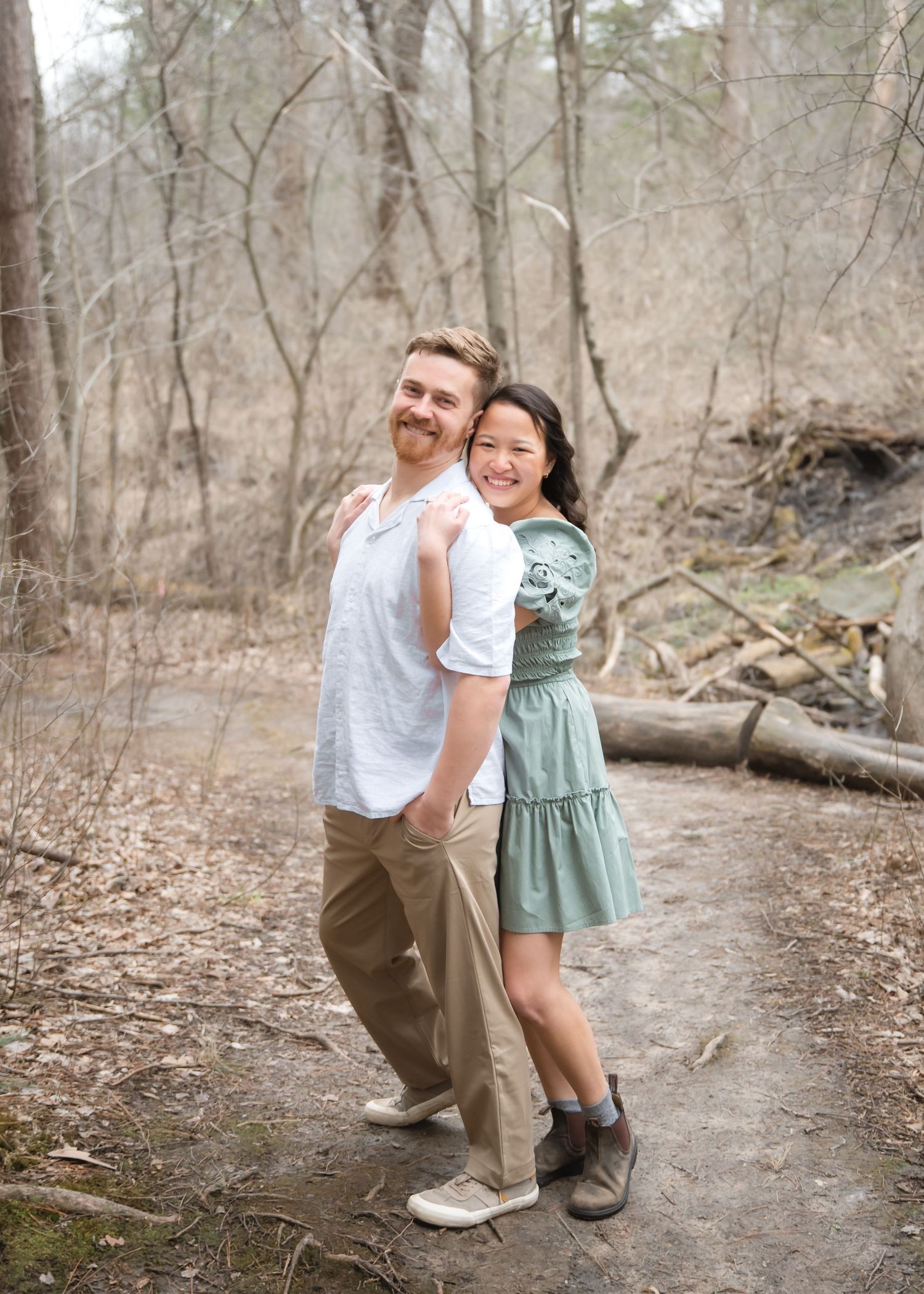 A couple shares a playful moment on a forest path during an engagement photo session in autumn.